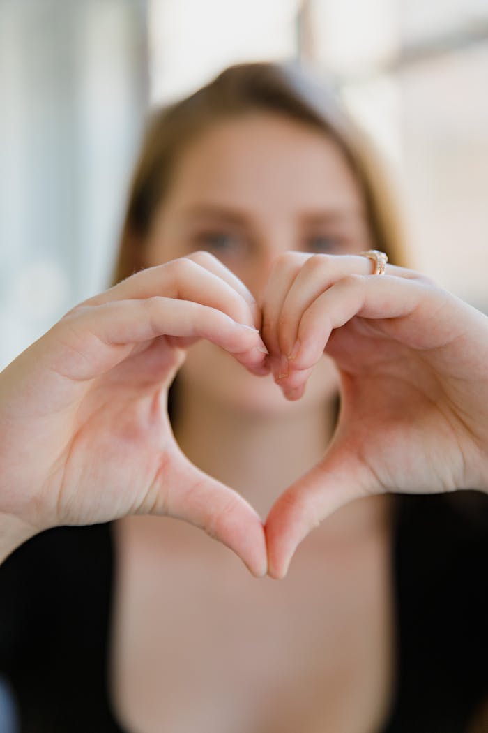 Close-up of a woman forming a heart shape with her hands, representing love and connection.