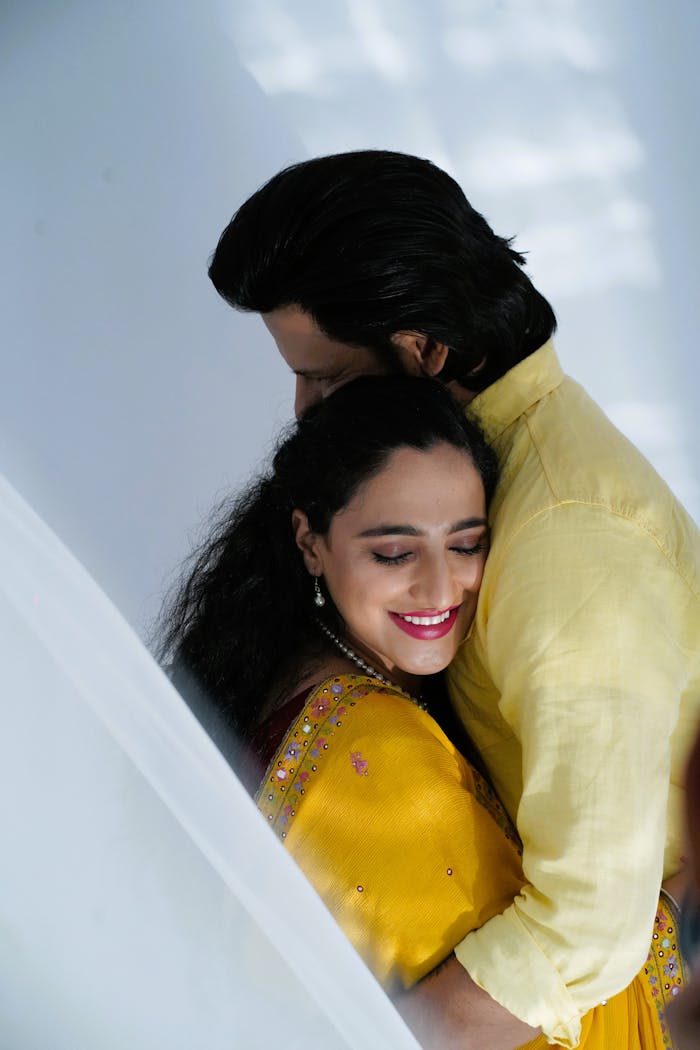 Happy couple in yellow clothes embracing indoors, showcasing love and togetherness.