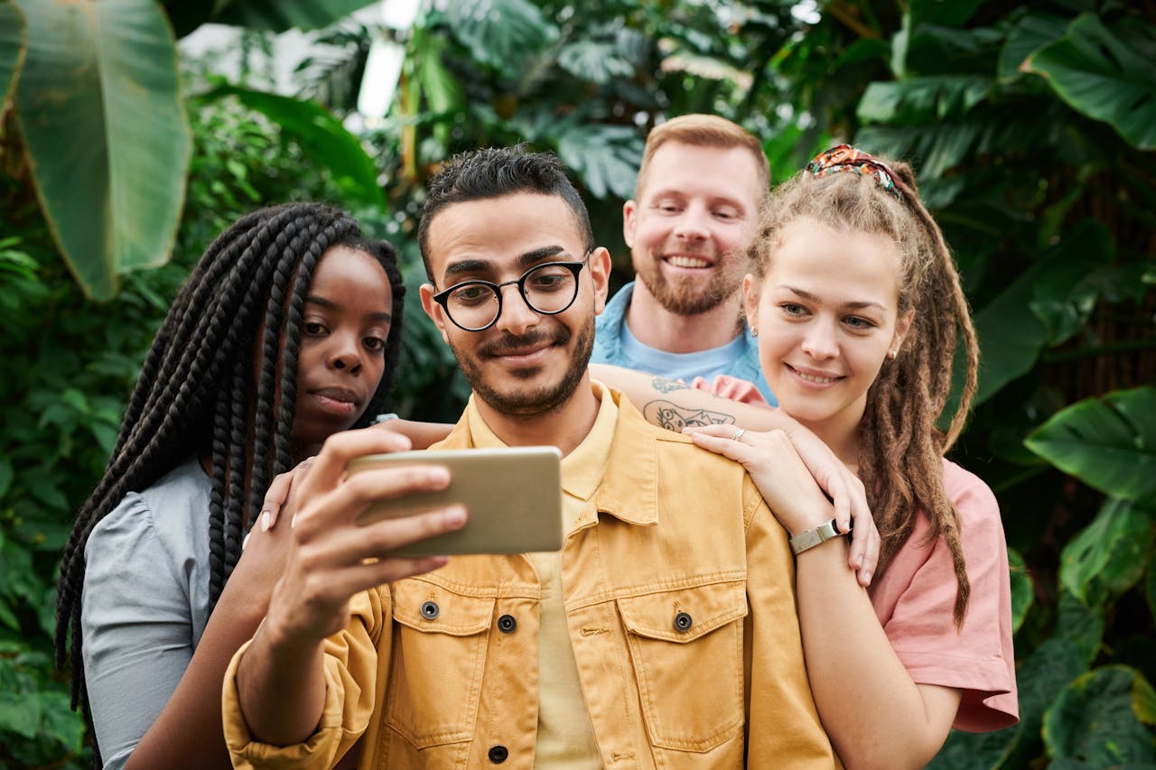 contact-img A group of four friends happily taking a selfie amidst lush greenery, capturing their joyful moments together.