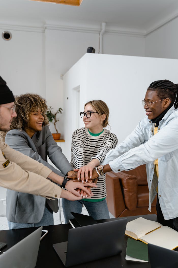 Diverse colleagues joining hands in a show of unity and teamwork in a modern office setting.