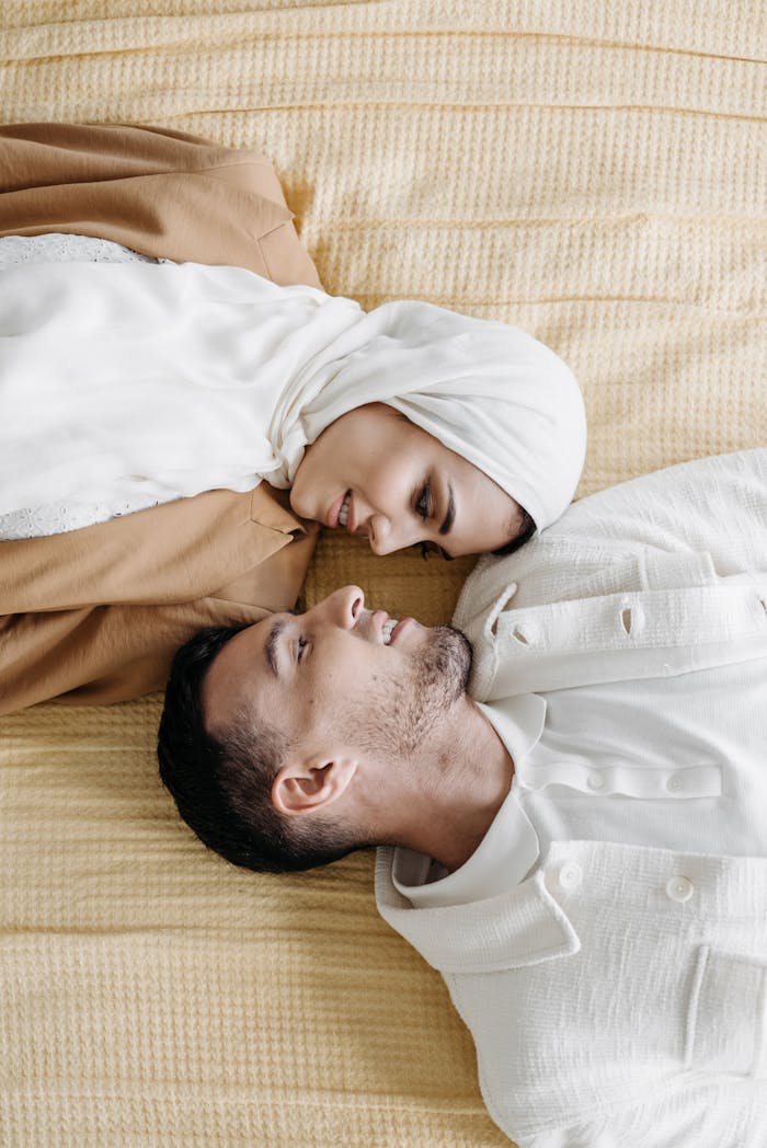 A loving couple gazing into each other's eyes on a soft bed with warm tones.